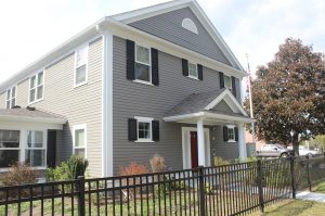 A gray two-story house with black shutters and a black fence around.