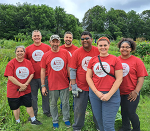 A groupshot of people in red shirts posing for a photo outside on a farm and smiling.