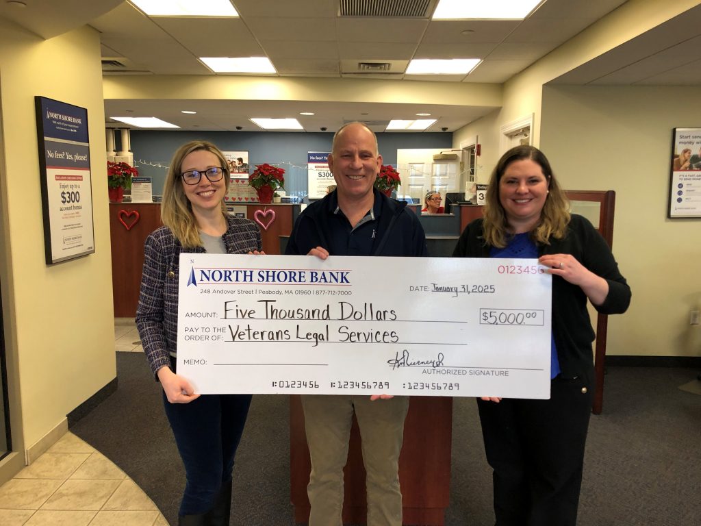 A group of bank employees holding a large check donation for Veteran's Legal Services. 